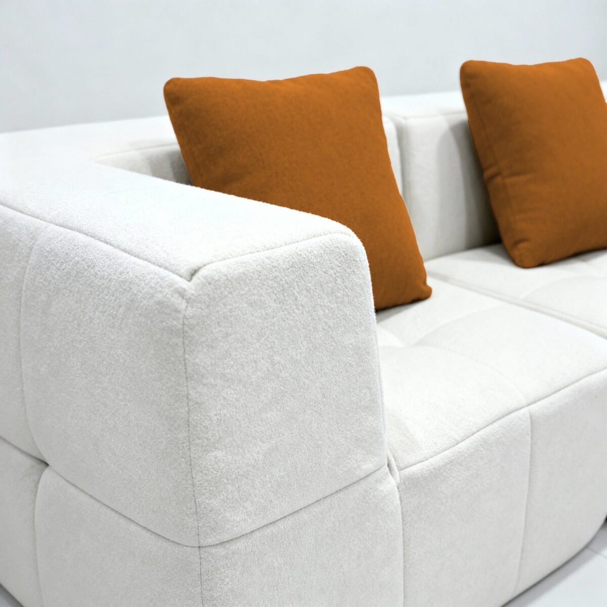 Canapé moderne blanc en tissu avec deux coussins décoratifs orange sur fond de mur clair