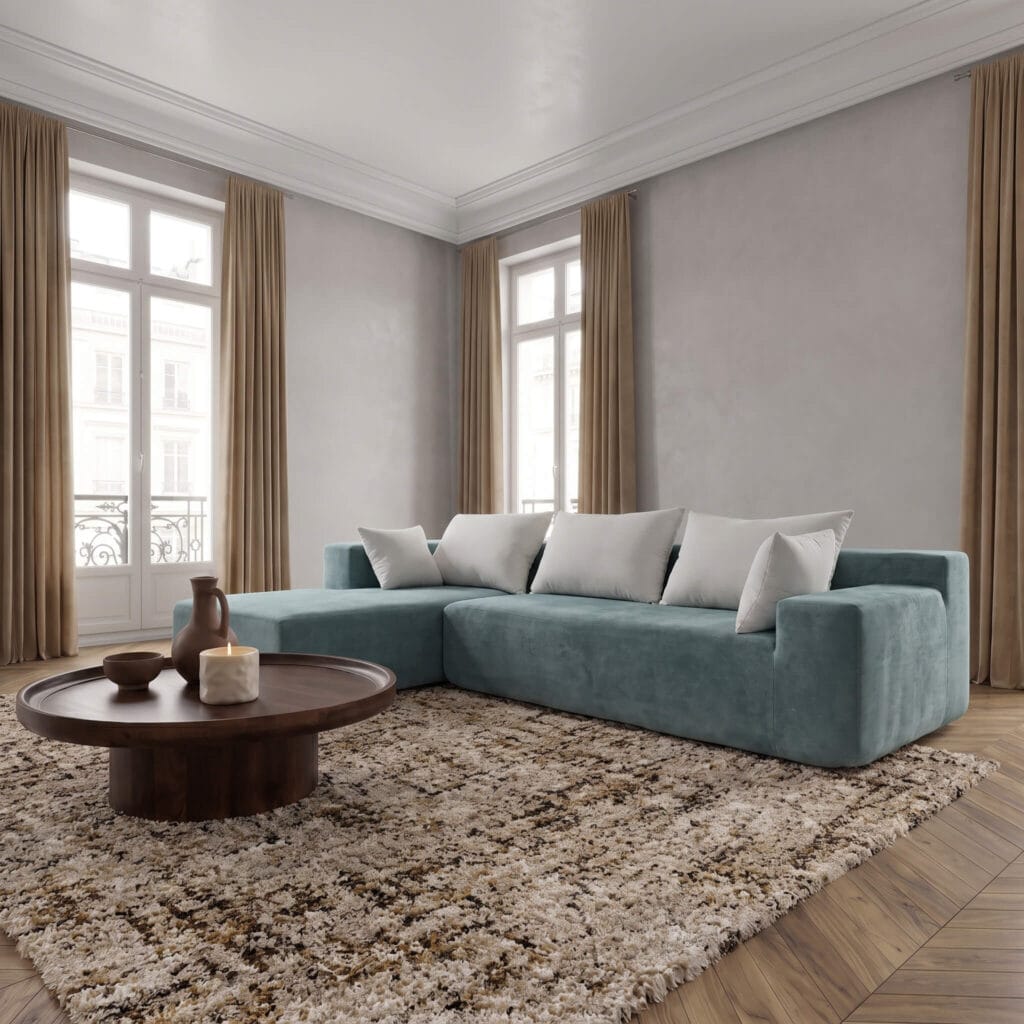 Un salon élégant avec canapé d'angle bleu canard, coussins gris, table basse ronde en bois sur tapis beige, parquet chevron et murs clairs.