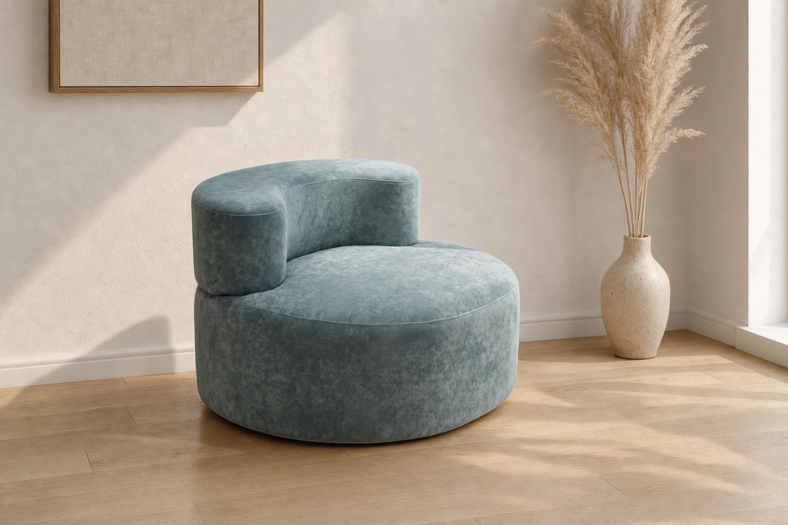 Fauteuil design Milo bleu-vert en tissu lisse installé dans un salon contemporain aux tons naturels avec mur blanc et parquet bois.