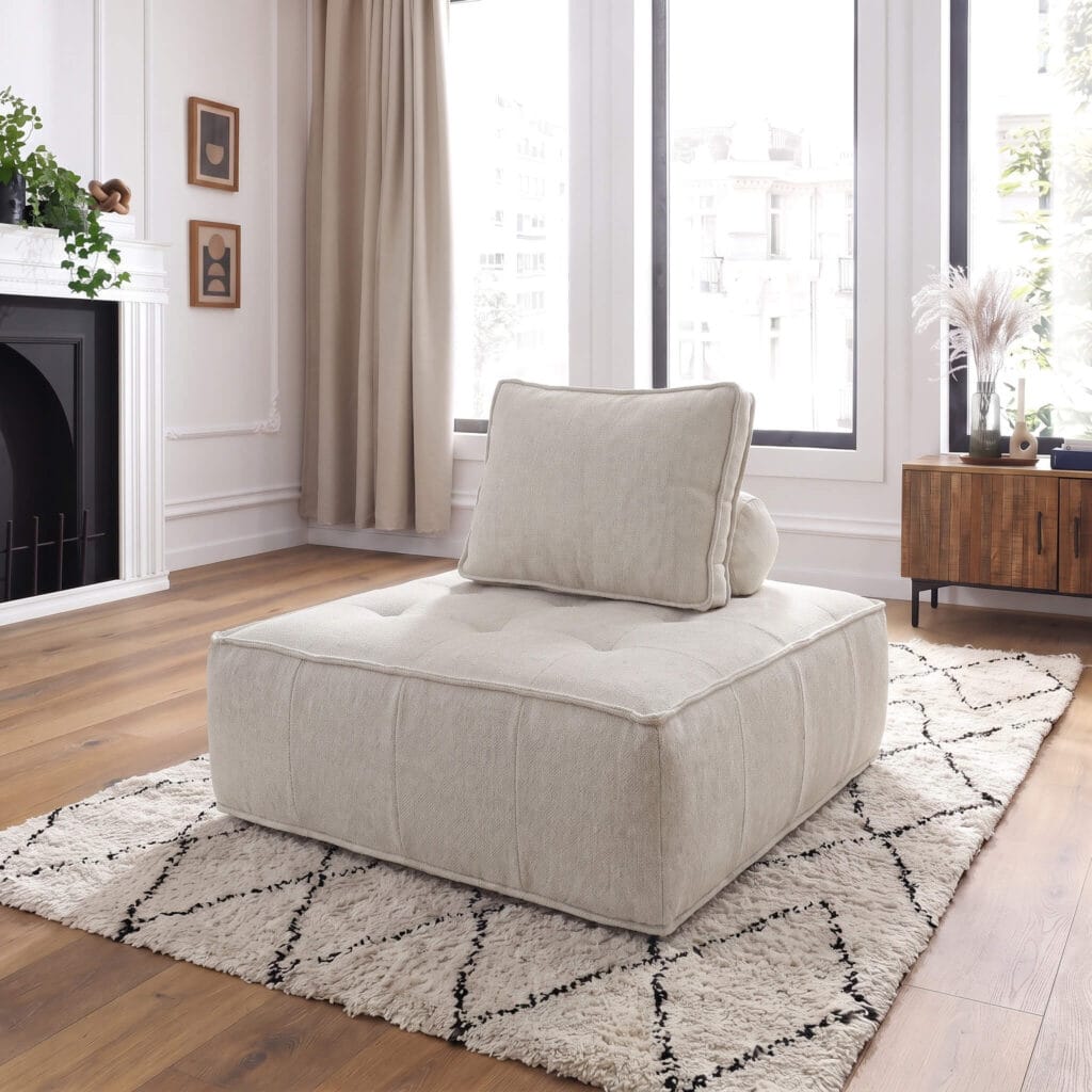 Un fauteuil modulable beige avec coussin d'appoint, posé sur un tapis berbère dans un salon lumineux au style contemporain et épuré avec cheminée.